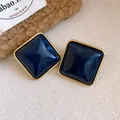 Primo piano di orecchini a lobo quadrati in acrilico blu scuro con bordo dorato - Stile con perno dell'orecchino in argento / Blu