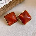 Detail von rotbraunen Acryl-Rautenohrsteckern mit elegantem goldfarbenem Metallrahmen. - Stil mit Silber-Ohrstecker / Orange
