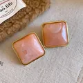 Dettaglio macro di orecchini a lobo quadrati in acrilico marmo rosa con cornice dorata - Stile con perno dell'orecchino in argento / Rosa