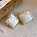 Dettaglio di eleganti orecchini a perno in acrilico con effetto marmo e bordo dorato - Stile con perno dell'orecchino in argento / Avorio