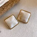Vista dettagliata di eleganti orecchini a lobo in acrilico marmorizzato con cornice dorata. - Stile con perno dell'orecchino in argento / Cachi
