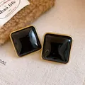 Macro di eleganti orecchini a lobo quadrati in acrilico nero con bordi in metallo dorato. - Stile con perno dell'orecchino in argento / Nero