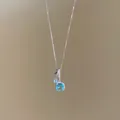 Gros plan d'un collier argenté orné d'un pendentif étincelant en zircon bleu carré. - Argent-Bleu