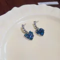 Close-up view of heart-shaped earrings with blue glass crystals and silver setting. - Stud Earrings / Stud Earrings (Blue)