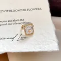 Macrodetail van een 18k vergulde rechthoekige zirkoon oorklem op getextureerd papier - Rechthoekige Zirconia Oorclip / Enkel Stuk / Goud