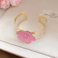 Primer plano de un brazalete dorado con un delicato colgante de flor en esmalte rosa - Bangle / Rosa