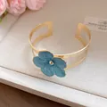 Close-up of an elegant gold double-band cuff bracelet featuring a blue enamel flower detail - Bangle / Blue