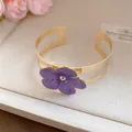Detalle macro de un elegante brazalete dorado con una flor de esmalte púrpura texturizada - Bangle / Púrpura