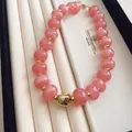 Makroansicht einer stilvollen rosa Katzenaugen-Perlenkette mit goldenem Quadratanhänger - Rosa
