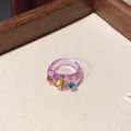 Detail view of a light purple resin ring with colorful embedded gemstones in a tray. - Purple And Brown