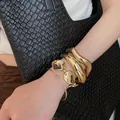Primo piano di bracciali rigidi dorati a strati in stile punk geometrico sul polso - Stile 49 / Set da 4 pezzi / Oro