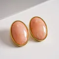 Close-up of vintage oval acrylic stud earrings with peach marble texture and gold trim - Pink