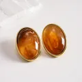 Detailed close-up of vintage amber acrylic oval stud earrings with gold metal frame - Coffee