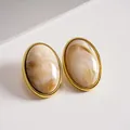 Close-up of retro oval geometric earrings with marbled acrylic and golden frames - Ivory