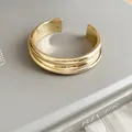 Detailed macro view of a minimalist gold metal open cuff bracelet with grooved texture - Smooth Layered Style / Gold
