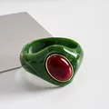 Vista dettagliata del bracciale rigido in acrilico verde marmorizzato con pietra rossa ovale. - Verde-Rosso