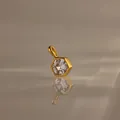 Zeshoekige heldere zirkoon hanger met gouden titanium stalen frame op spiegelend oppervlak. - April Geboortesteen Hanger