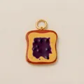Detailweergave van een acryl bedeltje in toastvorm met paarse jam en gouden ring. - Brood