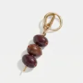 Nahaufnahme eines Oliven-Taschenanhängers mit roten Kristallen und goldfarbenem Verschluss - Braune Olive