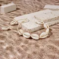 Dettaglio di un braccialetto di conchiglie con cordino intrecciato su travertino. - Bracciale Conchiglia Stile 5 / Beige