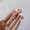 Detail shot of a pink cross pendant held between fingers showing its small size. - 6 Smooth Pendants