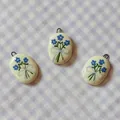 Macro view of oval ceramic jewelry pendants featuring hand-painted blue floral bouquets - Bowknot Pendant (9)