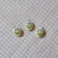 Close-up of oval ceramic pendants featuring hand-painted blue flowers and green leaves - 8 Oval Blue Flower Pendant