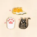 Set of three cute cat-themed enamel pins featuring a paw, black cat, and orange cat on a book - Cat Style(19)