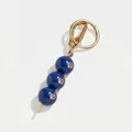 Vista dettagliata di un ciondolo per borsa con perle blu, anello oro e pietre viola - Oliva Blu Scuro con Pietra Viola