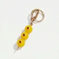 Detail van een gele fruitbedel voor tassen met goudkleurige ring en rode steenaccenten. - Gele Olijf