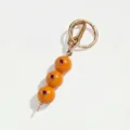 Detail van gouden sleutelhanger met drie oranje vruchtkralen en rode edelstenen. - Oranje Olijf