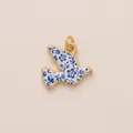 Close-up of a bird-shaped pendant with blue and white floral patterns and gold frame. - Dove Pendant