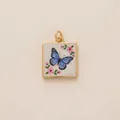 Macro detail of a square gold pendant featuring a blue butterfly and pink flowers. - Square Butterfly Pendant