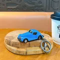 Creative blue alloy vintage car keychain accessory displayed on a wooden coaster in a cafe - Beetle Car Charm / Blue
