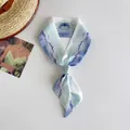 Close-up of artistic watercolor landscape silk scarf tied in a neat knot on white surface - Light Blue Landscape