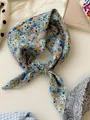 Detail shot of a blue floral cotton linen square scarf tied in a knot on white desk - 27 All-over Floral Blue Edge