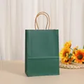 Detail of a dark green kraft paper gift bag with twisted rope handles in a warm setting. - Dark Green