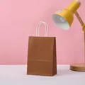 Detailed view of a minimalist brown kraft paper gift bag featuring sturdy white twisted paper handles - Brown