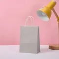 Minimalist gray kraft paper gift bag with white handles displayed in a warm home office setting - Gray