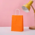 Detail view of a vibrant orange kraft paper gift bag with sturdy white twisted handles - Orange