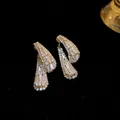 Elegante goudkleurige druppeloorbellen met fonkelende zirkonia op een zwarte achtergrond. - Goud