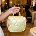 Vista detallada de un neceser amarillo acolchado con corazones sostenido por una modelo - Material PU Corazón Acolchado / 14.5*8.5*14.5cm / Amarillo