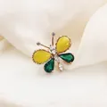 Elegant butterfly brooch with yellow and green stones on a soft white fabric. - KC0093