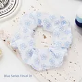 Close-up of a stylish white fabric scrunchie featuring delicate blue floral pattern details - Blue Flowers 2