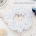 Macro view of a white fabric scrunchie with blue polka dots on a textured slab. - Blue Polka Dots 4