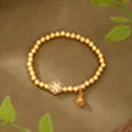 Close-up of an ancient gold beaded bracelet with a floral charm and bell accessory. - Floral Bell Bracelet (SL00248) / String of Beads / Gold