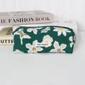 Close-up of green corduroy pencil case with white floral print and MAY RABBIT label - Green Background With White Butterfly Flowers