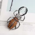 Vintage beetle brooch with orange and black rhinestones on a magazine background. - Brown