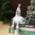 Detailed shot of a plush Christmas gnome ornament sitting on books with festive trees - Long Leg Doll / Gray
