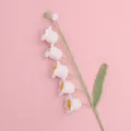 Detailed close-up of handmade white crocheted Lily of the Valley flower with green leaf. - White
